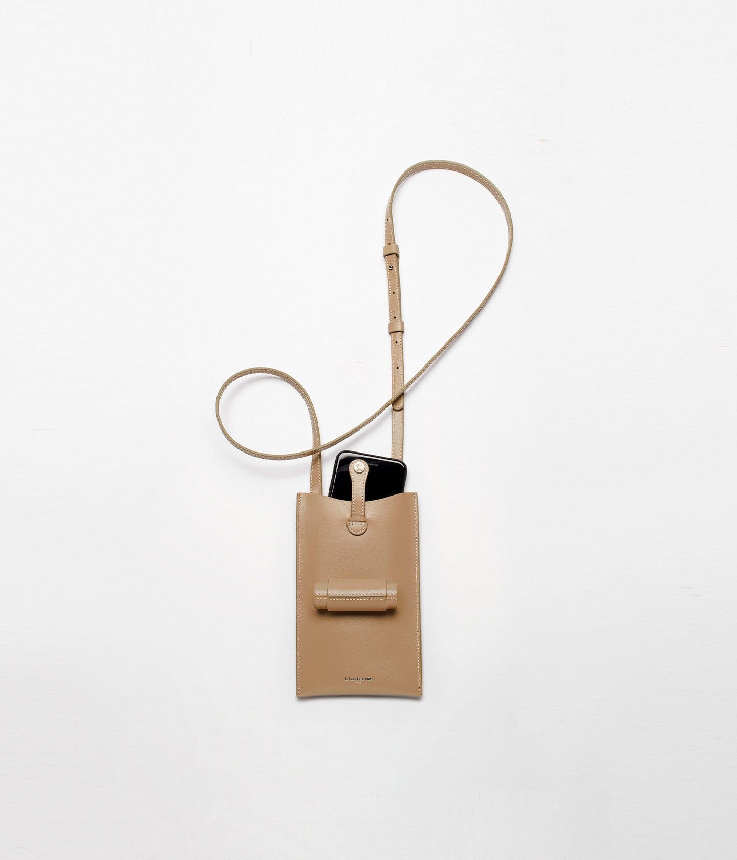 Sac Le 21 La Bouche Rouge Paris en cuir camel avec son écrin rechargeable et un téléphone placé à côté.