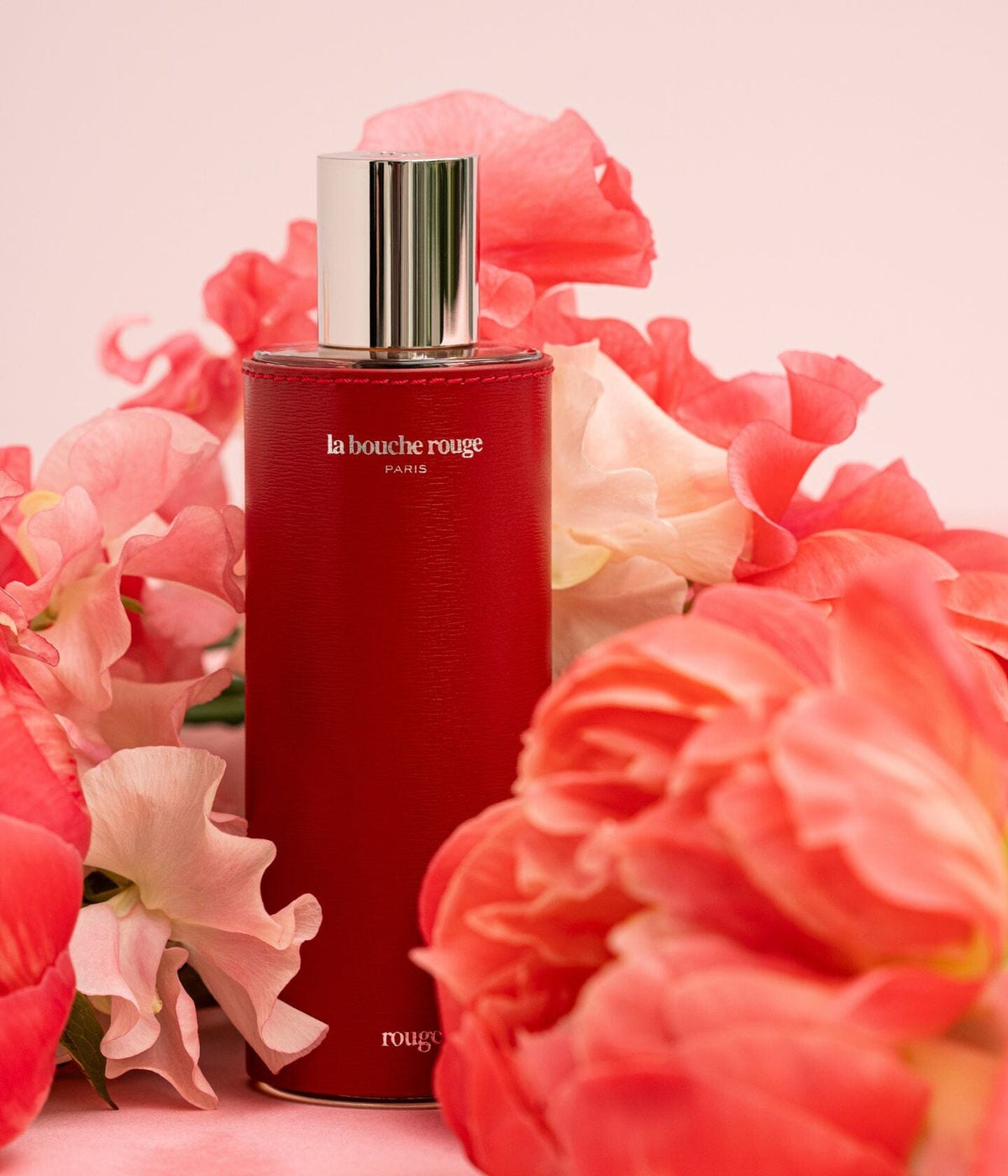 Rouge extrait de parfum by La Bouche Rouge Paris in a 100 ml bottle wrapped in red leather, with a floral arrangement