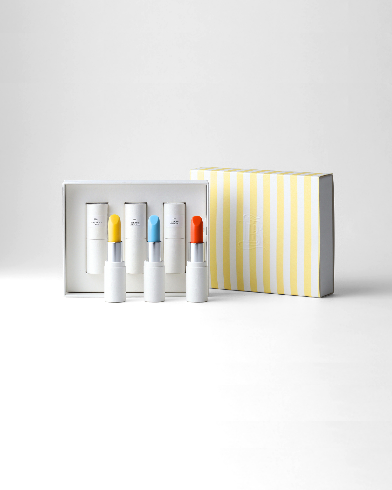 Coffret Dolce Vita La Bouche Rouge composé de trois baumes teintés transparents ouverts : Blu Cielo, Limoncello et Tangerino et le coffret rayé jaune et blanc
