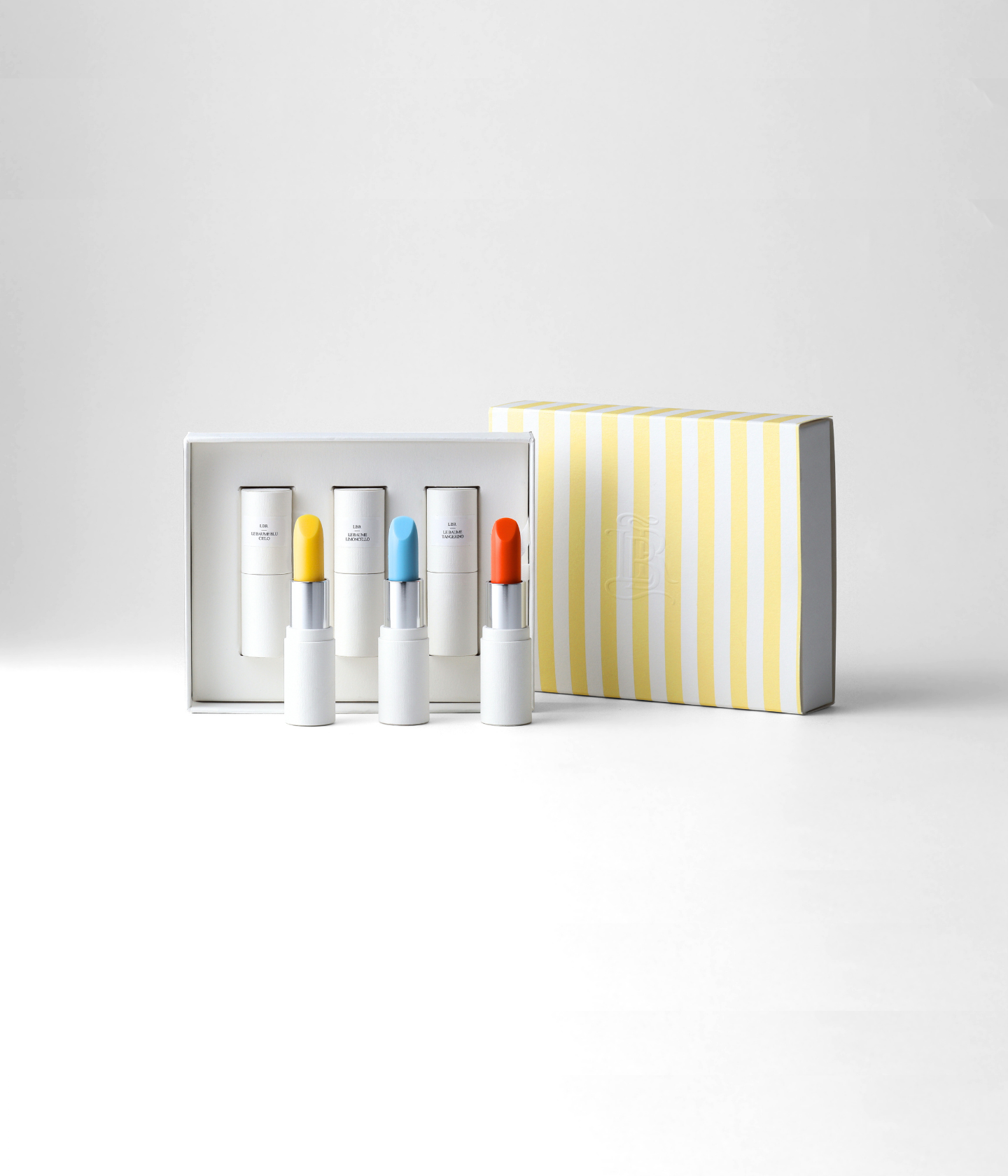 Coffret Dolce Vita La Bouche Rouge composé de trois baumes teintés transparents ouverts : Blu Cielo, Limoncello et Tangerino et le coffret rayé jaune et blanc